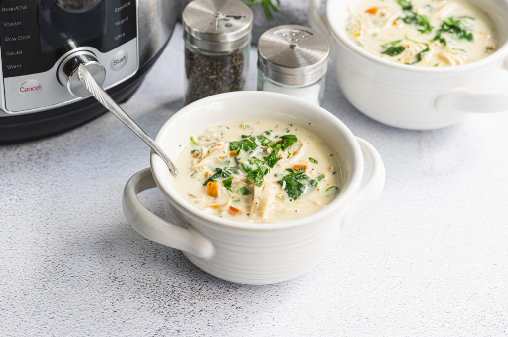 Two small bowls of creamy chicken gnocchi soup along with salt, pepper, and a multi-cooker.