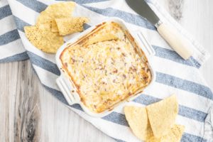Hot Cheddar Bacon Dip in a dish with chips around it