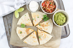 Cheesy Quesadillas cut into triangles and with sides of salsa, guacamole and sour cream