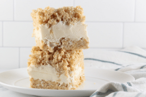 Two-layer crumb cake with creamy filling on a white plate, set against a white tiled background.