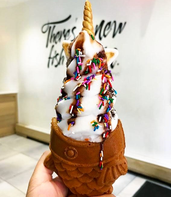 a fish shaped ice cream cone topped with a swirl of ice cream with a unicorn horn
