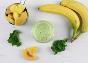 Peachy Green Pineapple Smoothie with bananas, peaches and spinach leaves around it