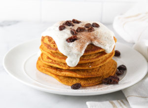 Pumpkin Pancakes in a tall stack with yogurt sauce and raisins on top