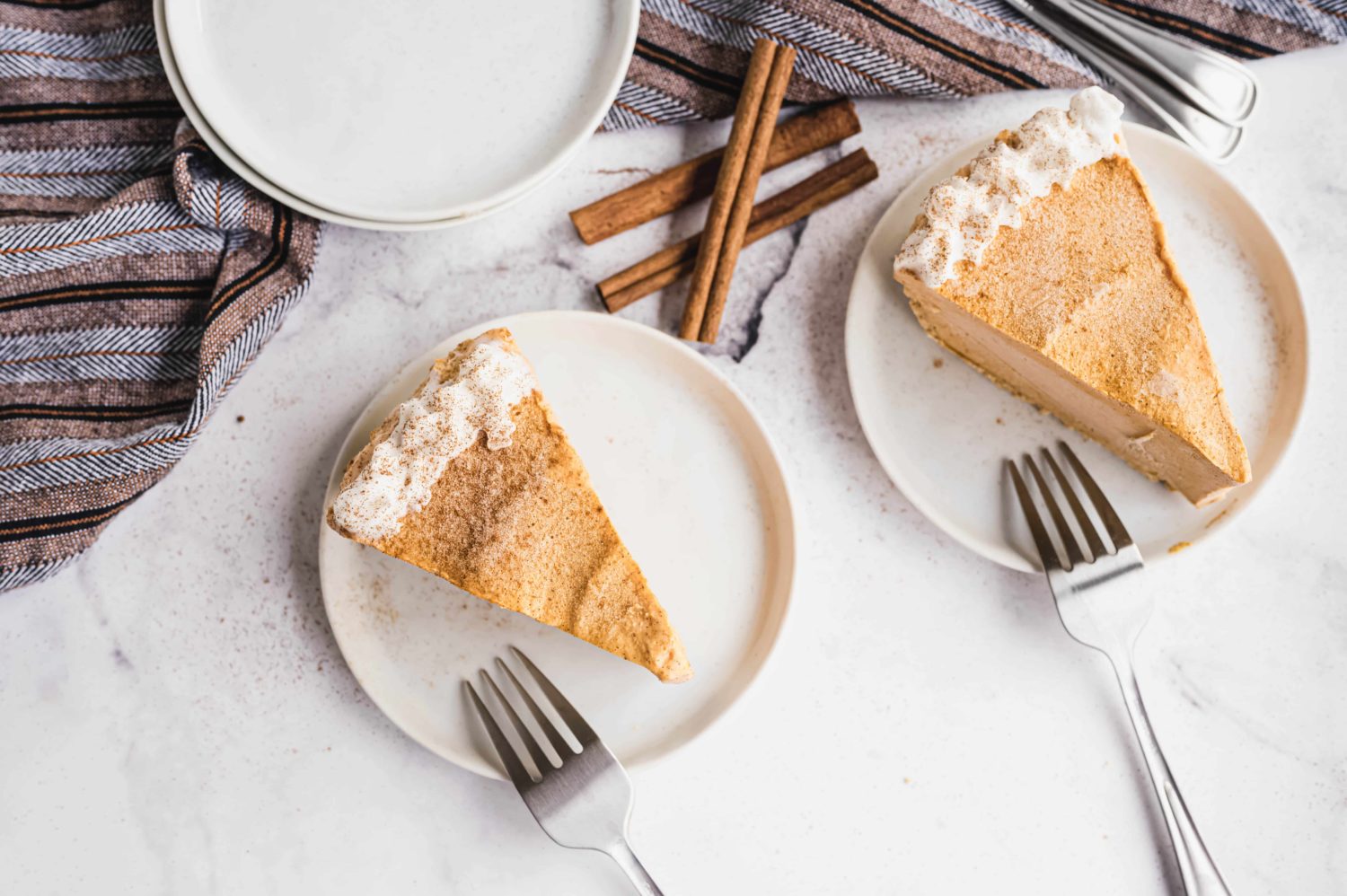 two slices of pumpkin praline cheesecake are pictured with cinnamon sticks and forks ready