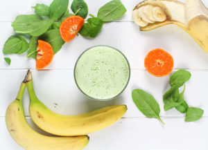 Spinach Orange Smoothie in a glass with spinach leaves, oranges and bananas around it.