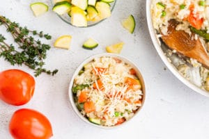 Summer Vegetable Risotto in a bowl with tomatoes, zucchini and spices around it