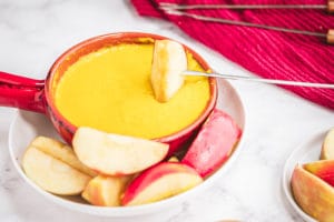 Swiss and Gouda Curry Fondue with an apple being dipped in it