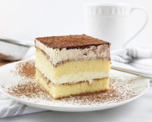 Tiramisu is pictured on a white plate with cinnamon sprinkled all around