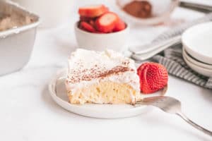 Tres Leche Cake slice on a plate topped with strawberries