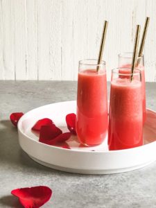 plate of 3 reddish pink smoothies in fancy glasses with rose petals and gold straws