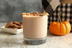 cocktail in a candy rimmed glass against a pumpkin and fall themed background