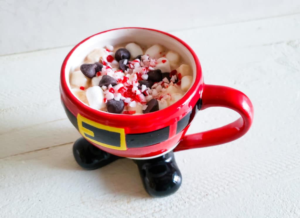a santa mug filled with marshmallows, chocolate chips and candy cane crumbs