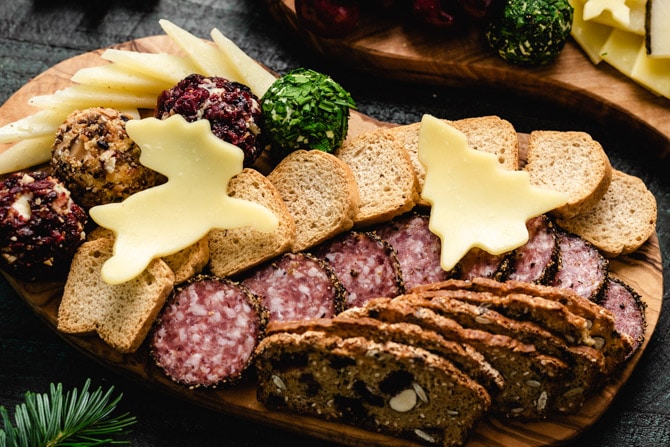 a reindeer and tree shaped piece of cheese on top of meats and breads for a cheese board
