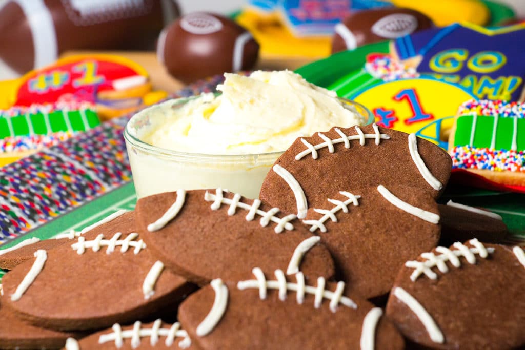 Chocolate Football Cookies with Cream Cheese Frosting Dip in a pile with football party decorations