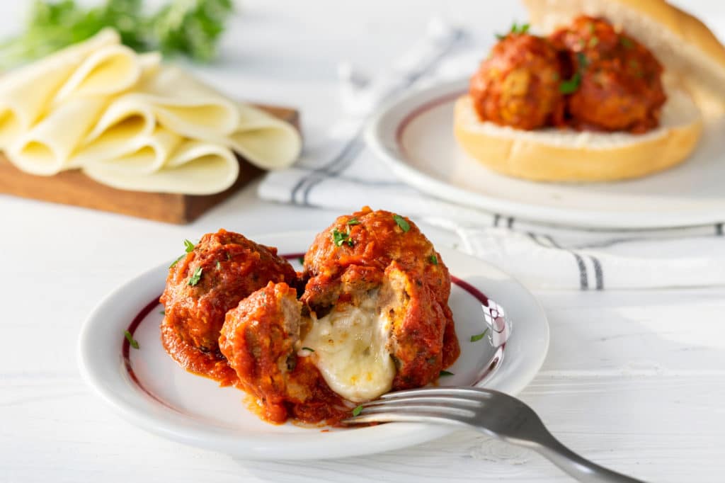 Slow Cooker Mozzarella Stuffed Meatballs - one has been sliced open so you can see the cheese inside.