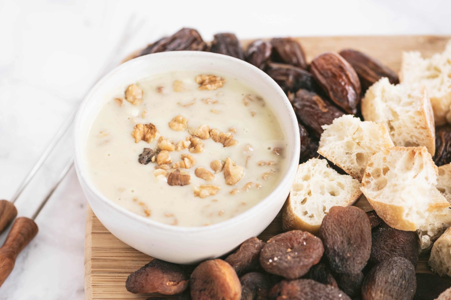 a bowl of light colored fondue with dates and pecans sprinkled on and around it