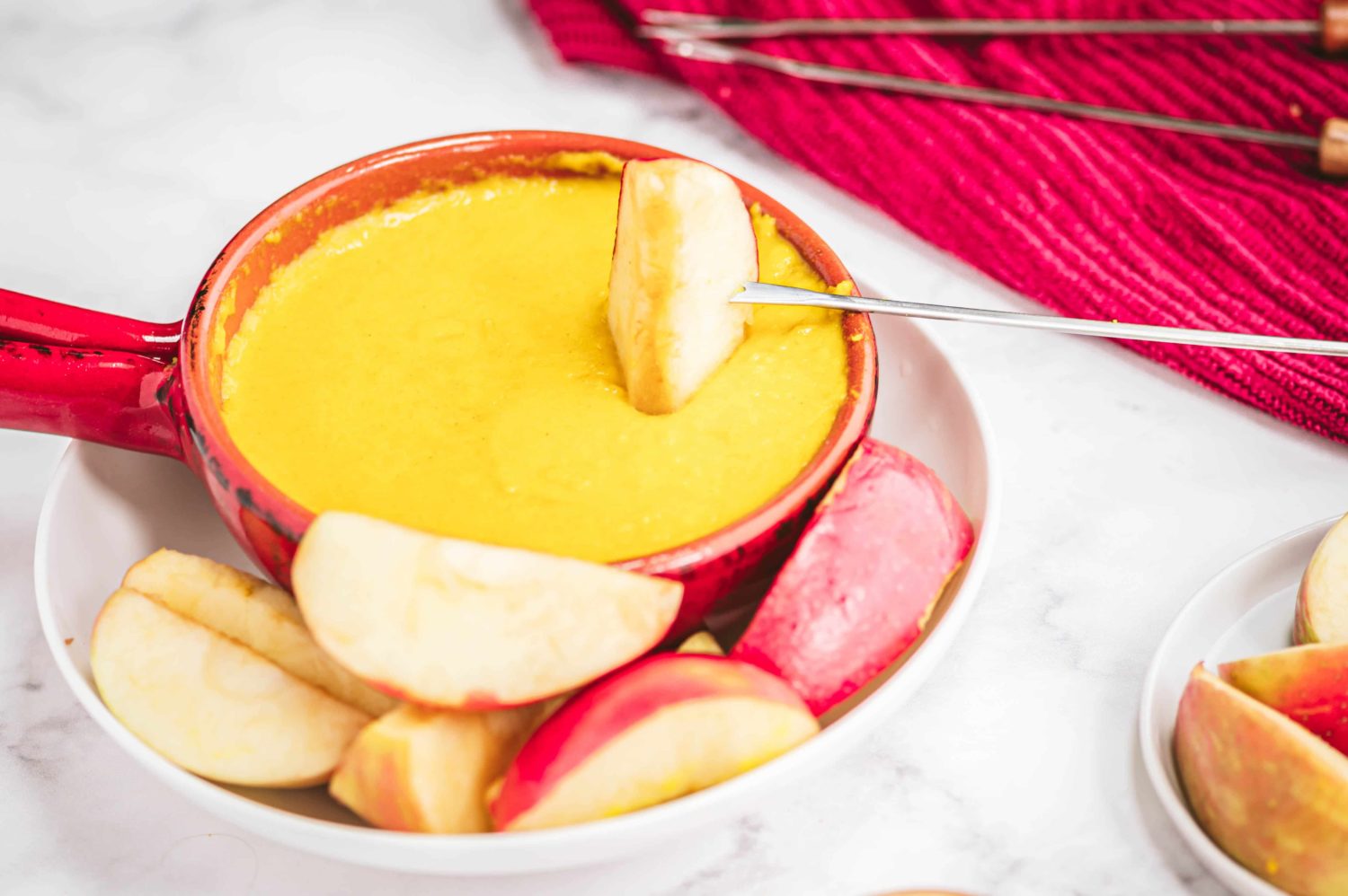 a bowl of fondue cheese that is bright yellow with an apple being dipped in
