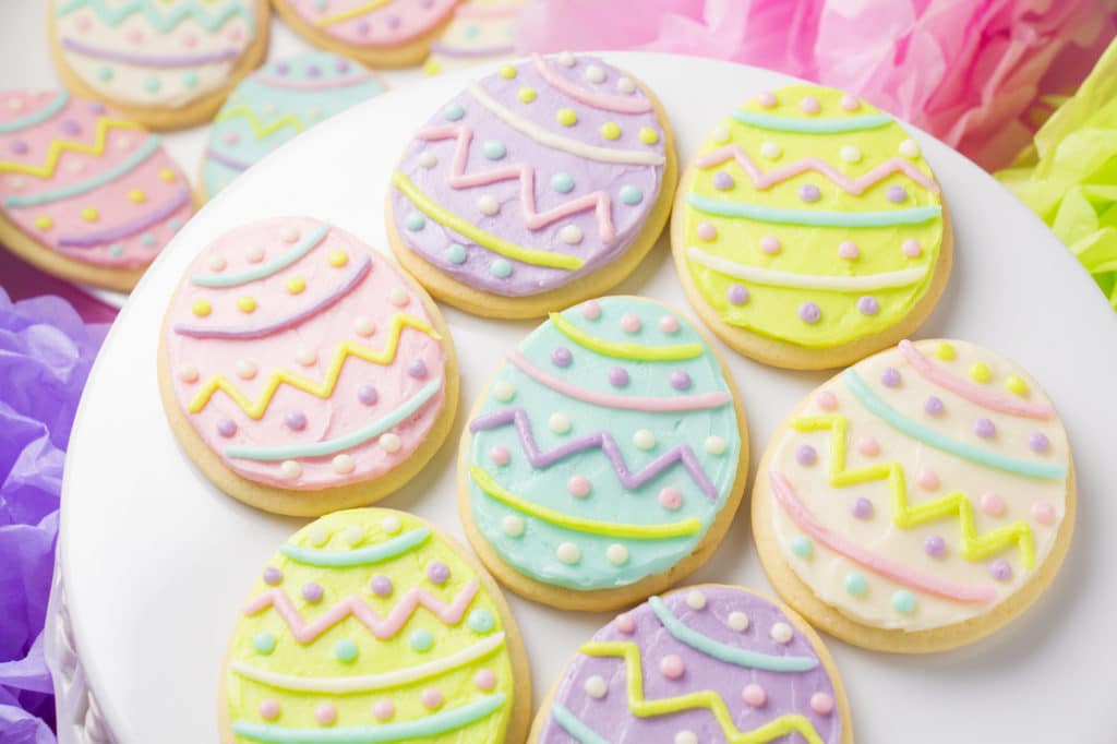 Easter egg cookies decorated with buttercream frosting on a white tray.