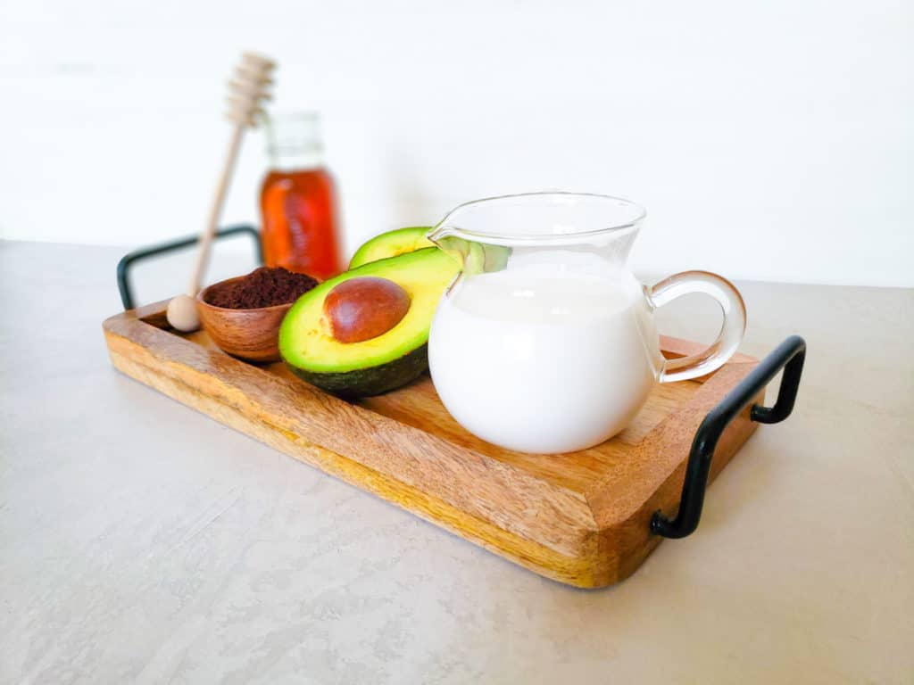wooden serving tray with milk, avocado and honey on it