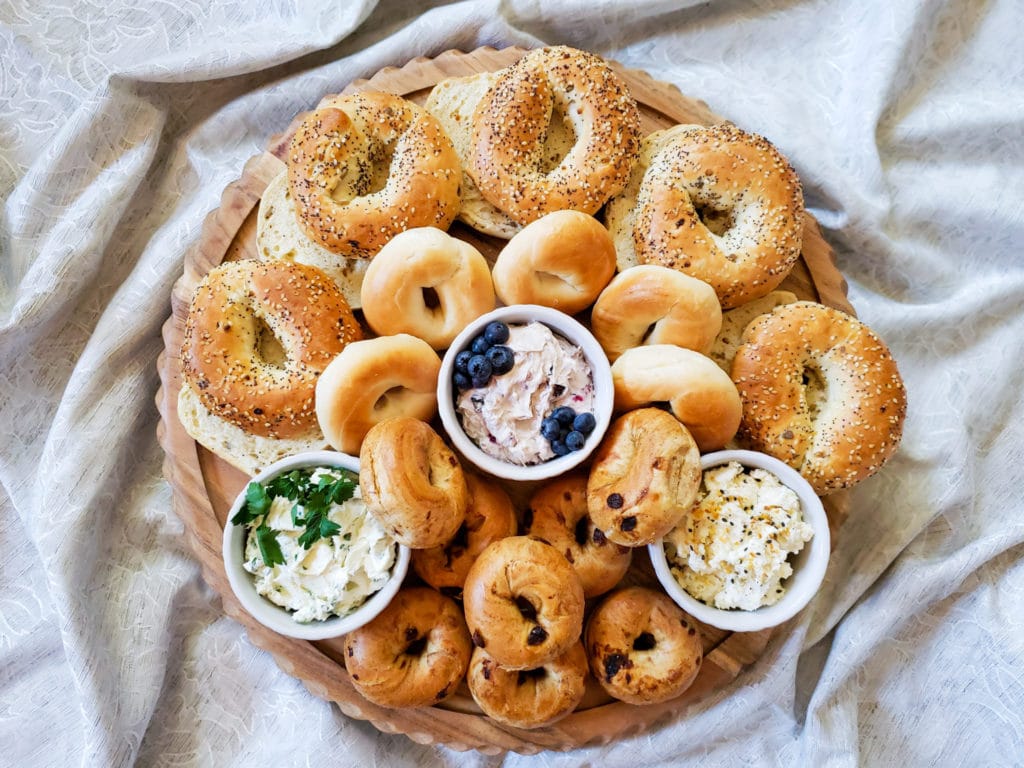 bagel board with various sizes and flavors of bagels and 3 different dips