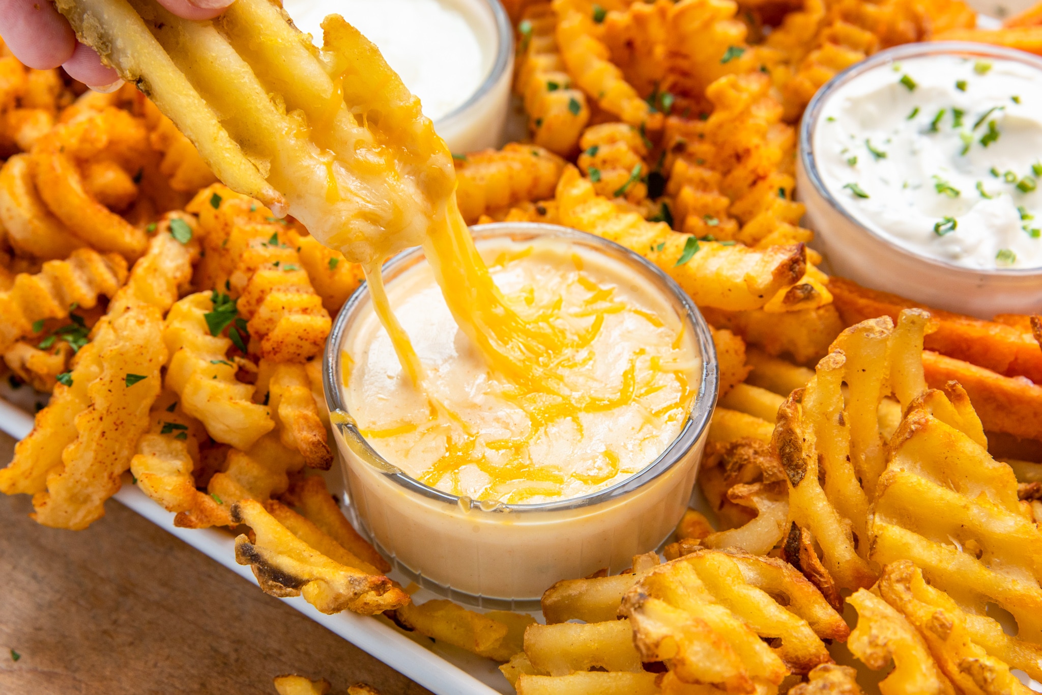 A finger dipping a waffle fry in taco cheese dip, creating a perfect combination of flavors.