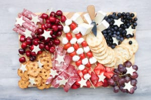A patriotic charcuterie board featuring assorted cheeses, cold cuts, and fruits, adorned with decorative cheese stars