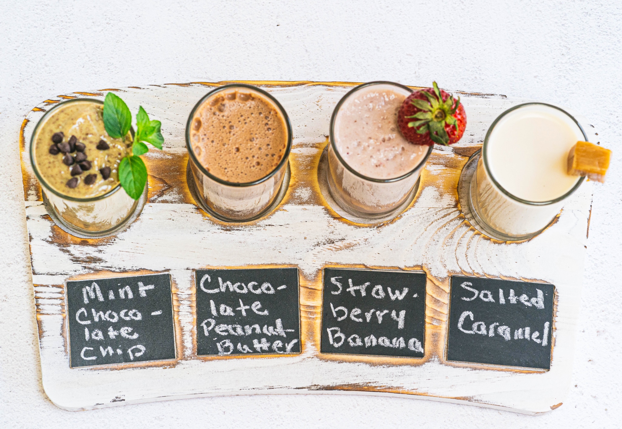 a wooden serving board with 4 glasses of different flavored milk on it. 