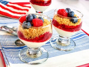 two fancy glasses with mini no bake cheesecakes in them topped with granola and berries.