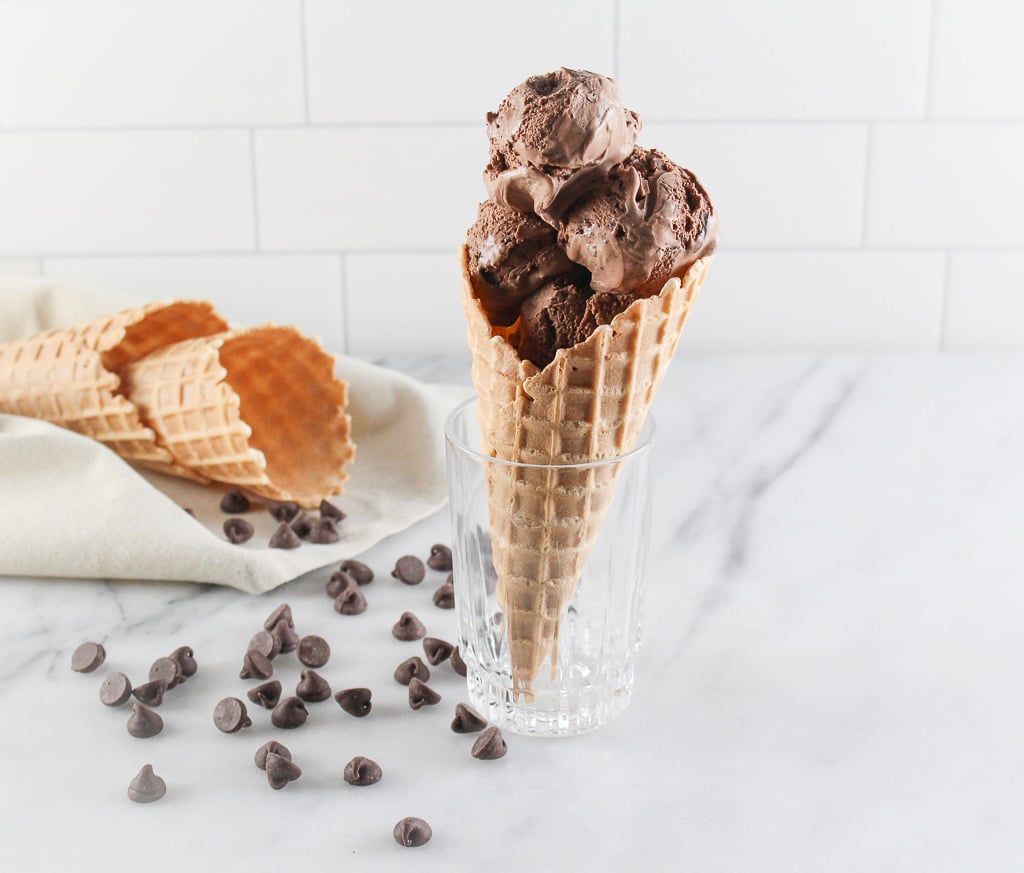 a waffle cone of chocolate ice cream in a glass so it stands up