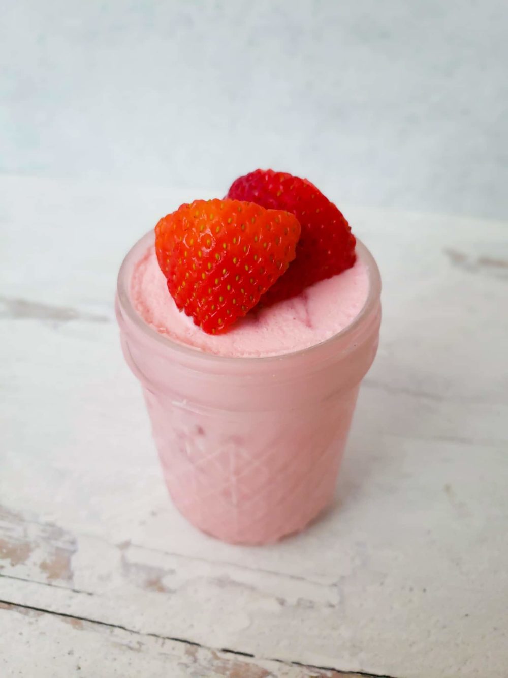 pink ice cream in a small mason jar with strawberries on top