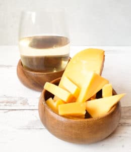 glass of white wine with a wooden bowl of cheese slices