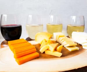 three glasses of wine, 2 white and one red with 3 types of cheese