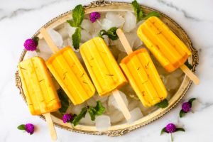Tropical Mango Lassi Ice Pops on a serving tray garnished with green leaves and purple flowers