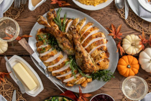 Herb and Parmesan Crusted Turkey on a serving dish surrounded by decorative pumpkins and a dish of butter