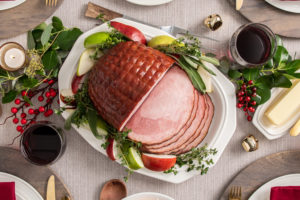 Maple-Bourbon Glazed Ham on a white serving dish and surrounded by festive red berries and apples