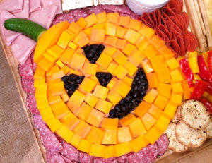 halloween charcuterie board with cheese cubes and olives making a jack-o-lantern