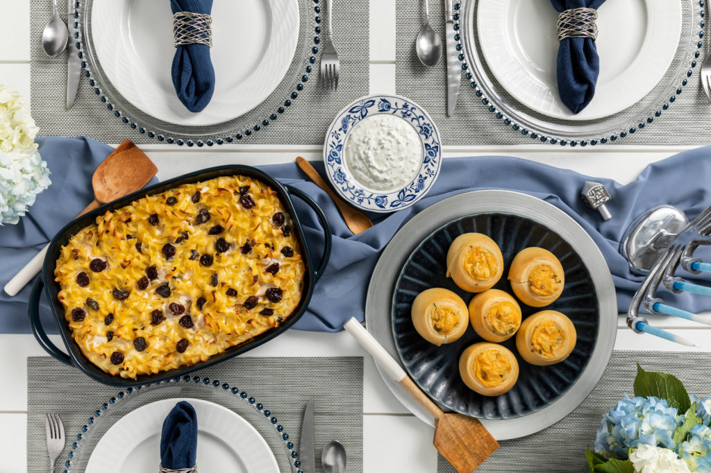 A Hanukkah-themed table with typical foods including kugel and potato knish and a dip dish.
