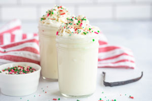 two glasses of Vanilla Holiday Cookie Milk topped with whipped cream and red and green sprinkles