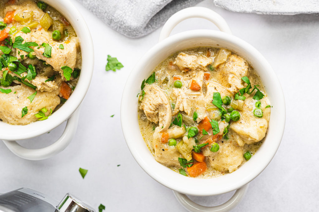 chicken and dumplings in a small white dish garnished with greens