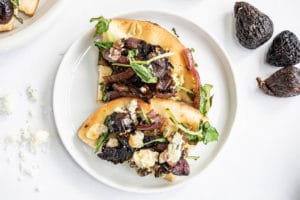 two slices of Nothing better than a new flatbread recipe to mix up pizza night! Caramelized Onion, Fig and Blue Cheese Flatbread on a white plate and garnished with greens