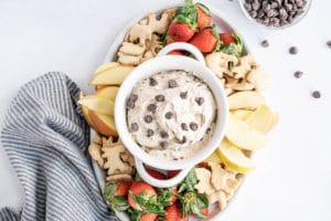 a bowl of Peanut Butter Chocolate Chip Cookie Dough Dip surrounded by cut fruit and animal crackers