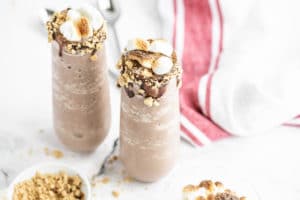 a glass of chocolate shake topped with marshmallows and graham cracker crumbs
