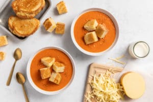 two bowls of fire-roasted tomato bisque with grilled cheese croutons on top