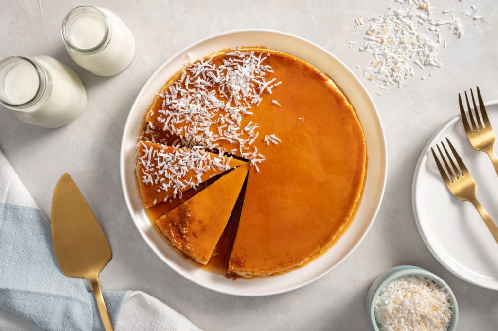Flan de Coco in a white dish with gold silverware and coconut sprinkled on top