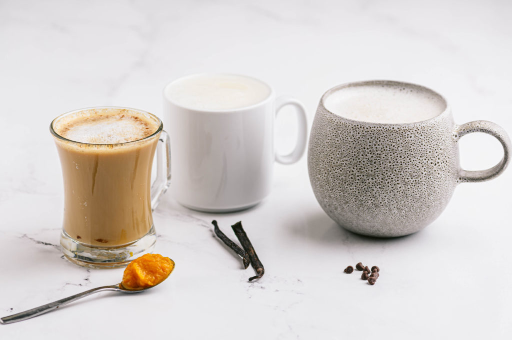 Three different versions of lattes ready to enjoy accompanied by a spoonful of pumpkin syrup.