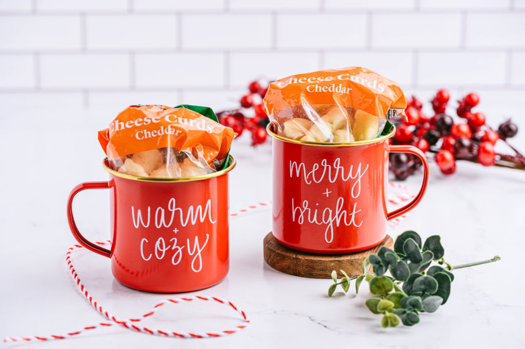 Bags of cheddar cheese curds inside a pair of festive red mugs next to holiday decorations.