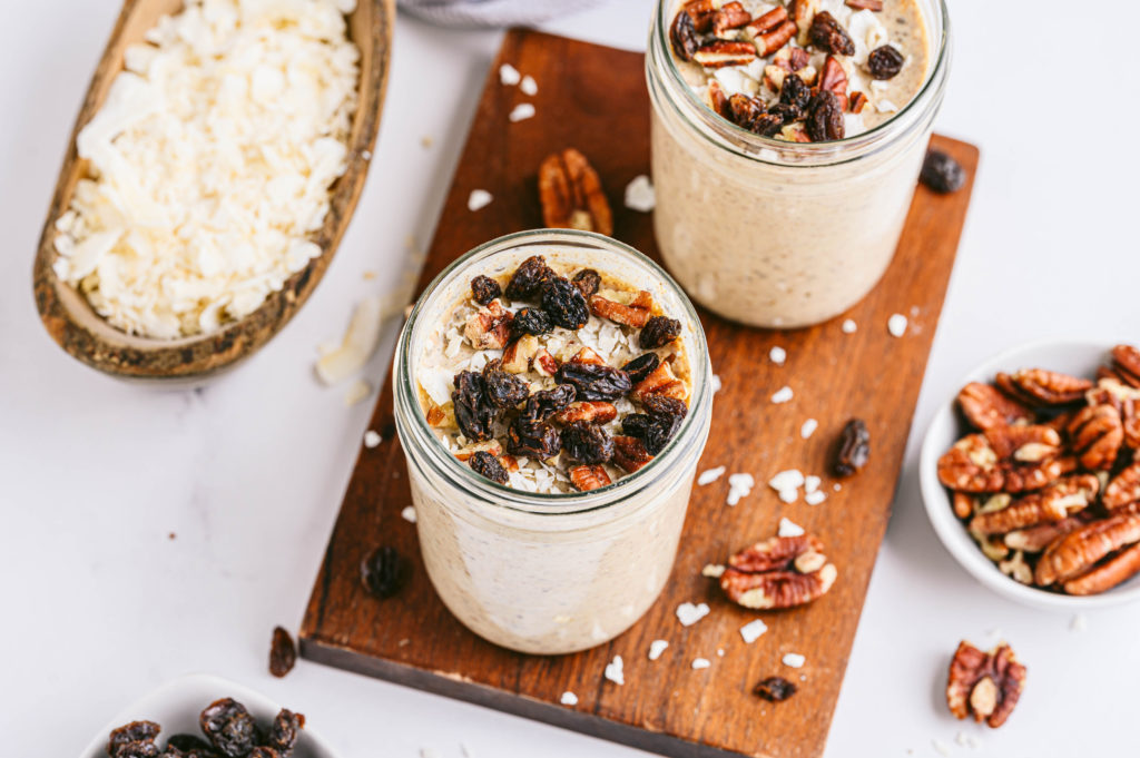 Two mason jars filled with gingerbread creamy overnight oats topped with almonds and raisins.