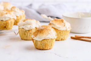 Three snickerdoodle muffins with creamy yogurt frosting over a white table.