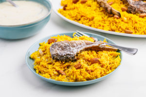 Piece of masaf lamb chop over yellow rice with almonds on a blue ceramic plate.
