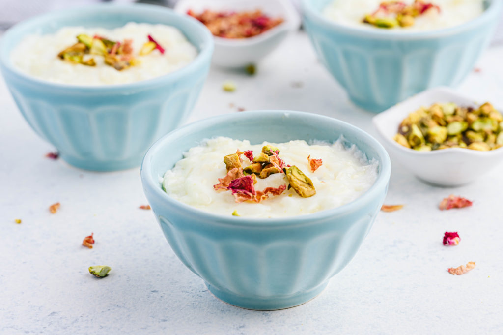 Riz bi Haleeb served in blue bowls garnished with pistachios and rose petals.